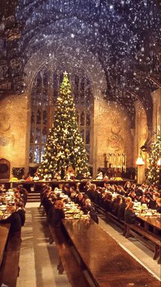 people are sitting at tables in front of a christmas tree with snow falling on it