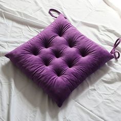 a purple square cushion sitting on top of a white sheet