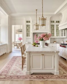 a kitchen with white cabinets and pink flowers on the island