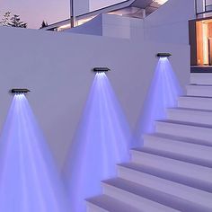 three lights on the side of a white building next to some steps and stairs in front of a house