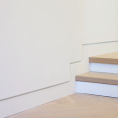 a cat sitting on top of some steps next to a white wall and wooden floor