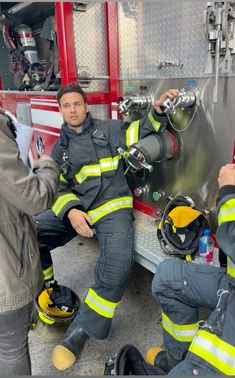 two firemen are sitting on the ground and one is holding his hand out to another man