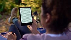 a woman sitting on the ground holding an electronic device in her hand and reading it