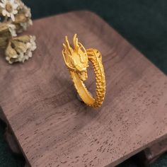 a gold dragon ring sitting on top of a wooden table next to flowers and a vase