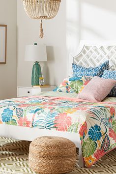 a bed with colorful sheets and pillows on top of it next to a table lamp