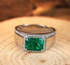 an emerald and diamond ring sitting on top of a piece of wood