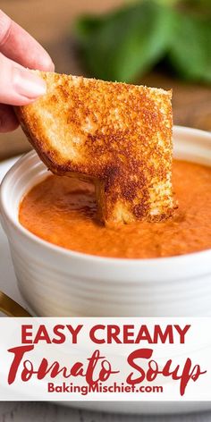 a hand dipping some bread into a bowl of tomato soup