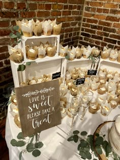 a table topped with lots of cupcakes next to a sign that says love is sweet please take a treat