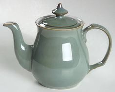 a green teapot with a lid and handle on it's side, sitting against a white background