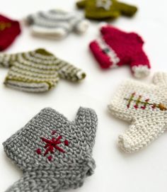 knitted mittens and gloves are arranged on a white surface, including one with red cross