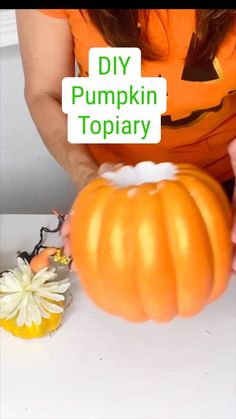 a woman in an orange shirt is decorating a pumpkin