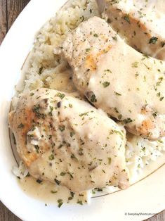 chicken with gravy and rice on a white plate sitting on a wooden table