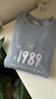 a grey sweatshirt with the year 1989 printed on it sitting on a table next to a potted plant