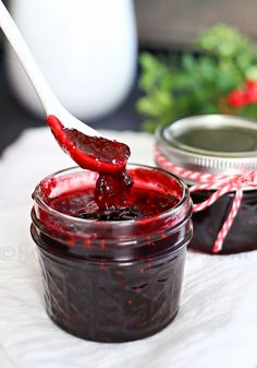 a spoon full of jam sitting on top of a white napkin next to two jars filled with jam