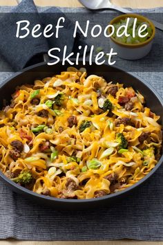 a skillet filled with beef noodle and broccoli on top of a table