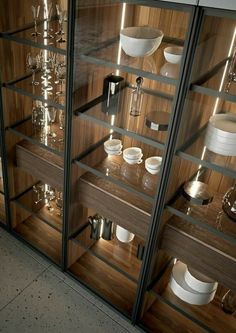 a glass display case filled with white dishes and silverware on top of wooden shelves