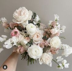 a bouquet of white and pink flowers is being held by someone's hand against a gray wall