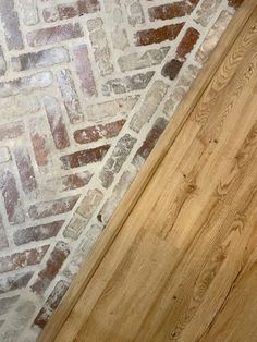 a cat is sitting on the floor next to a door and a brick wall with wood trim