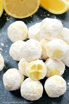 some lemons are next to some snowball cookies on a black surface with powdered sugar