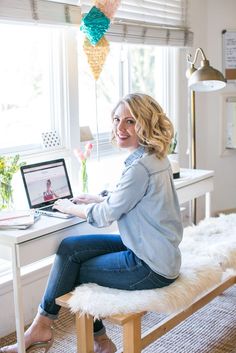 a woman sitting at a desk with a laptop and flowers in front of her window