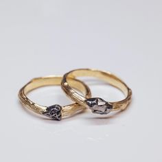 two gold wedding rings with black diamonds on each one, set against a white background