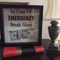 an emergency break glass sign on a table next to some books and a lamp with the words in case of emergency