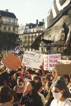 a large group of people holding signs and wearing face masks in front of some buildings