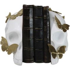 a white skull with gold butterflies sitting next to two black books