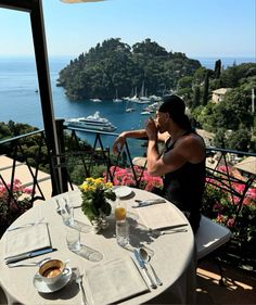 a man sitting at a table with food and drinks in front of an ocean view