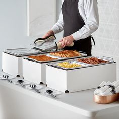 a man in an apron preparing food on top of a buffet table with utensils