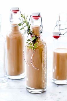 three bottles filled with liquid sitting on top of a counter next to glasses and spoons