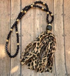 a leopard print necklace with black beads and a brown beaded tassel on a wooden surface