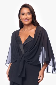 a woman wearing a black dress with sheer sleeves and a tie around the waist, smiling at the camera