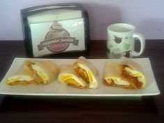 three sandwiches are on a plate next to a coffee cup and toasted sandwich box