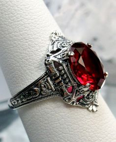 Simulated Red Ruby Ring Cleopatra Design#209 Custom Made To Order   This is a stunning Art Deco reproduction ring in sterling silver. The flawless simulated oval full cut red ruby gemstone is 10mm x 8mm. The setting is 18mm North to South on the finger. The inside of the band is marked 925 for solid sterling silver. The beautiful filigree is a mixture of Egyptian Revival and Art Deco design. There is   lovely swirl patterns in the geometric design.  Take an imaginary trip down the Nile river and Oval Ruby Ring With Intricate Design, Ornate Round Ruby Ring, Red Gemstone Ring For Ceremonial Occasions, Red Gemstone Rings For Ceremonial Occasion, Ceremonial Red Gemstone Ring, Red Oval Victorian Jewelry, Wedding Ruby Ring With Intricate Design, Victorian Style Red Oval Jewelry, Victorian Style Red Round Rings