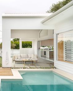 an empty swimming pool in front of a white house with a couch and table next to it