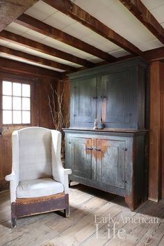 an old chair sitting next to a wooden cabinet in a room with exposed wood beams