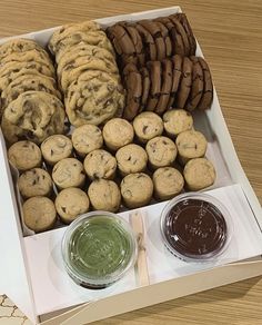 an open box filled with cookies and other desserts next to two jars of chocolate