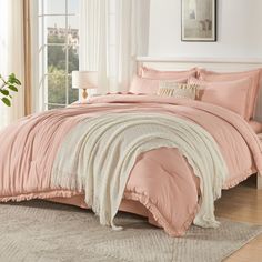 a bed with pink comforter and pillows in a room next to a white window