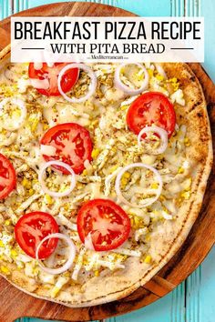 a pizza topped with tomatoes and onions on top of a wooden cutting board next to a blue wall