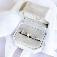 two wedding rings sitting in a box on top of a white cloth covered bed sheet