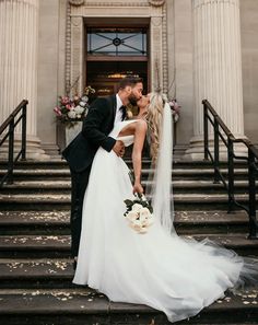 a bride and groom kissing on the steps of an old building