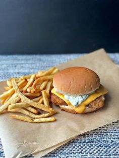 a chicken sandwich with cheese and fries on a piece of wax paper next to it