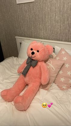 a large pink teddy bear sitting on top of a bed next to pillows and hearts