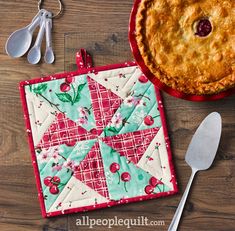 a pie sitting on top of a wooden table next to a pot holder and spoon