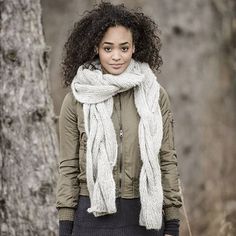 a woman standing in front of a tree wearing a white scarf and black leggings