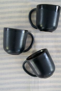 three black coffee mugs sitting on top of a white and blue striped table cloth