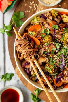 a bowl filled with noodles, carrots and broccoli next to chopsticks