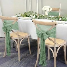 the table is set with two chairs and one has green sashes on it, along with white flowers