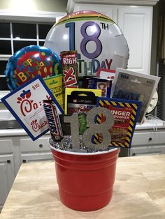 a red bucket filled with lots of different items and balloons in the shape of numbers